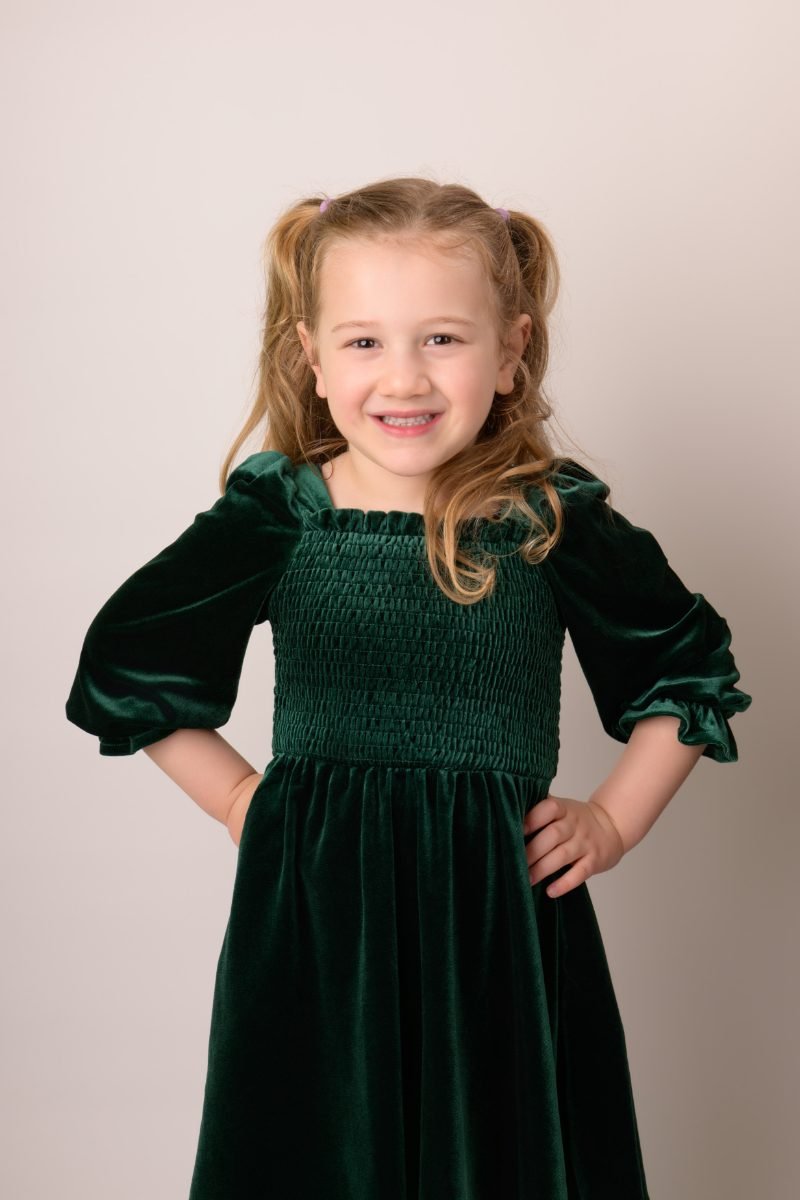 A girl in a green velvet dress smiling at the camera