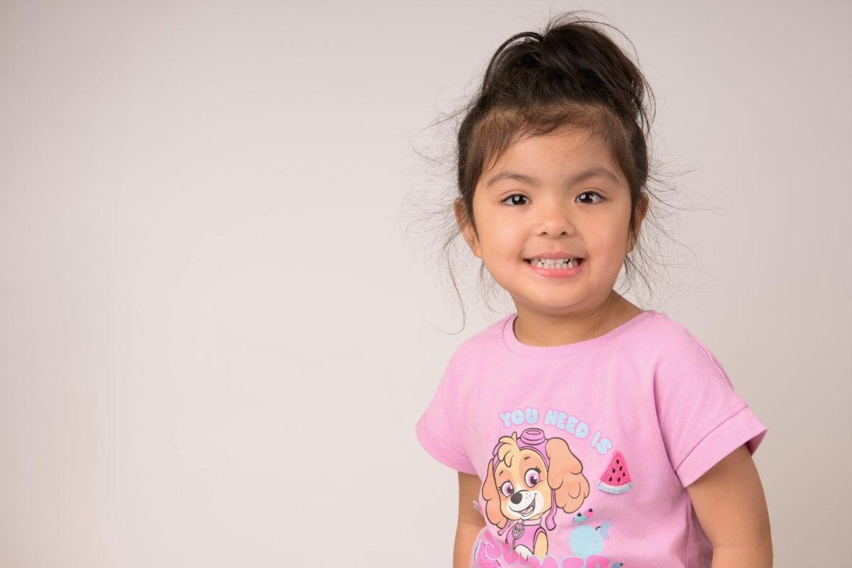 A girl in a pink cartoon tee with one hand raised