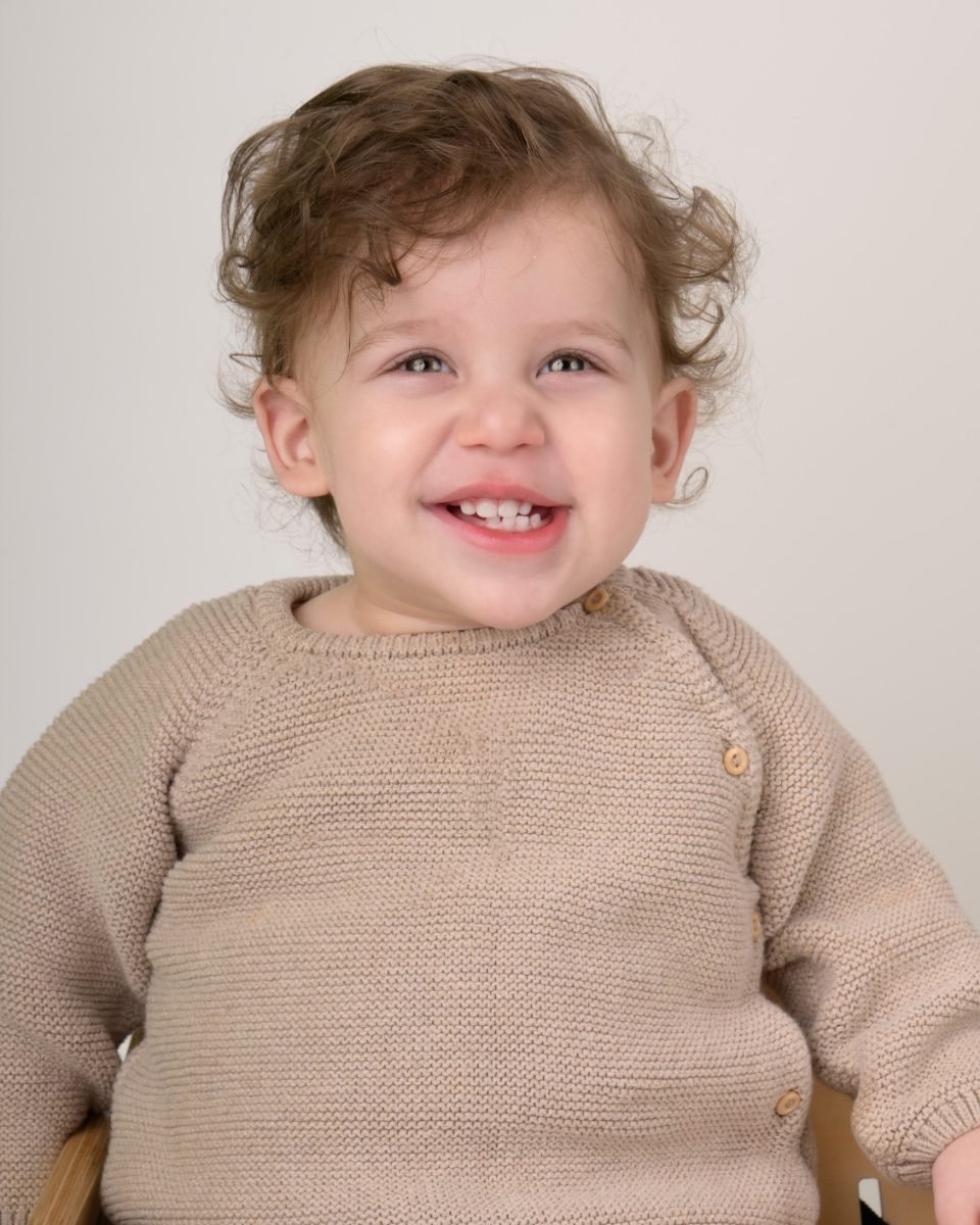 A curly-haired toddler boy in a cream knit sweater