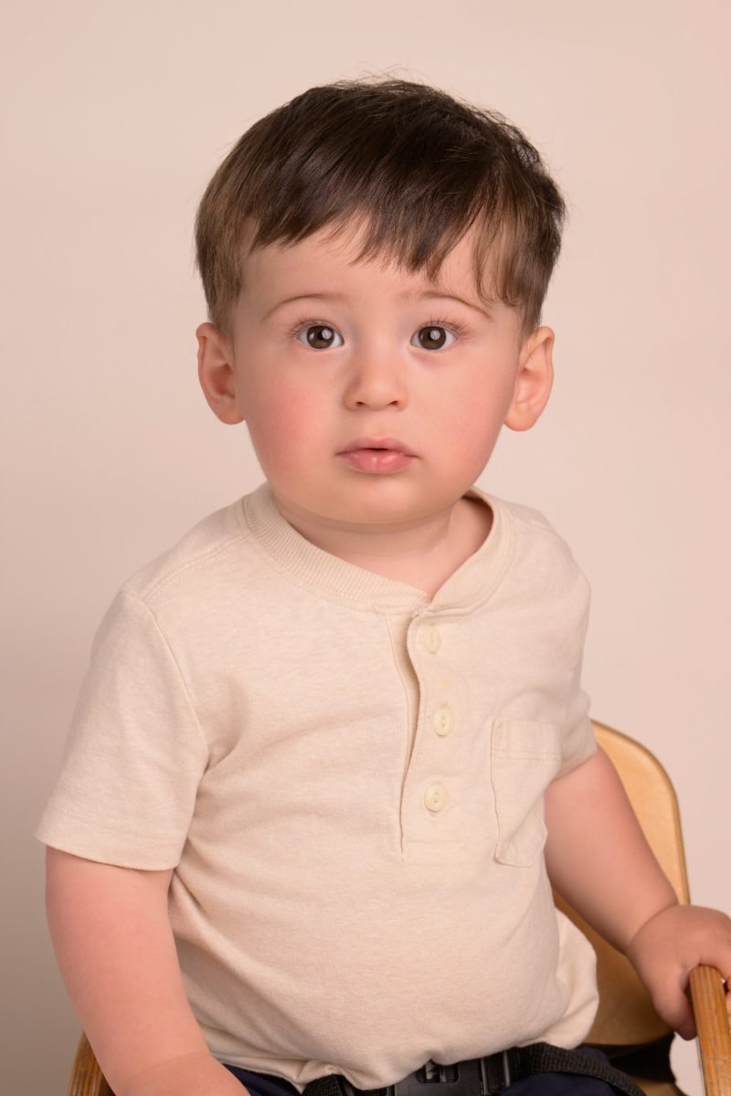 A toddler boy in a cream henley on a warm neutral backdrop