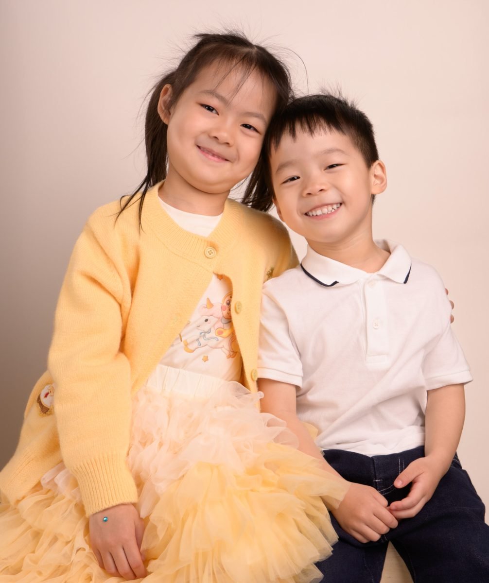 A sister in a yellow cardigan standing beside her little brother