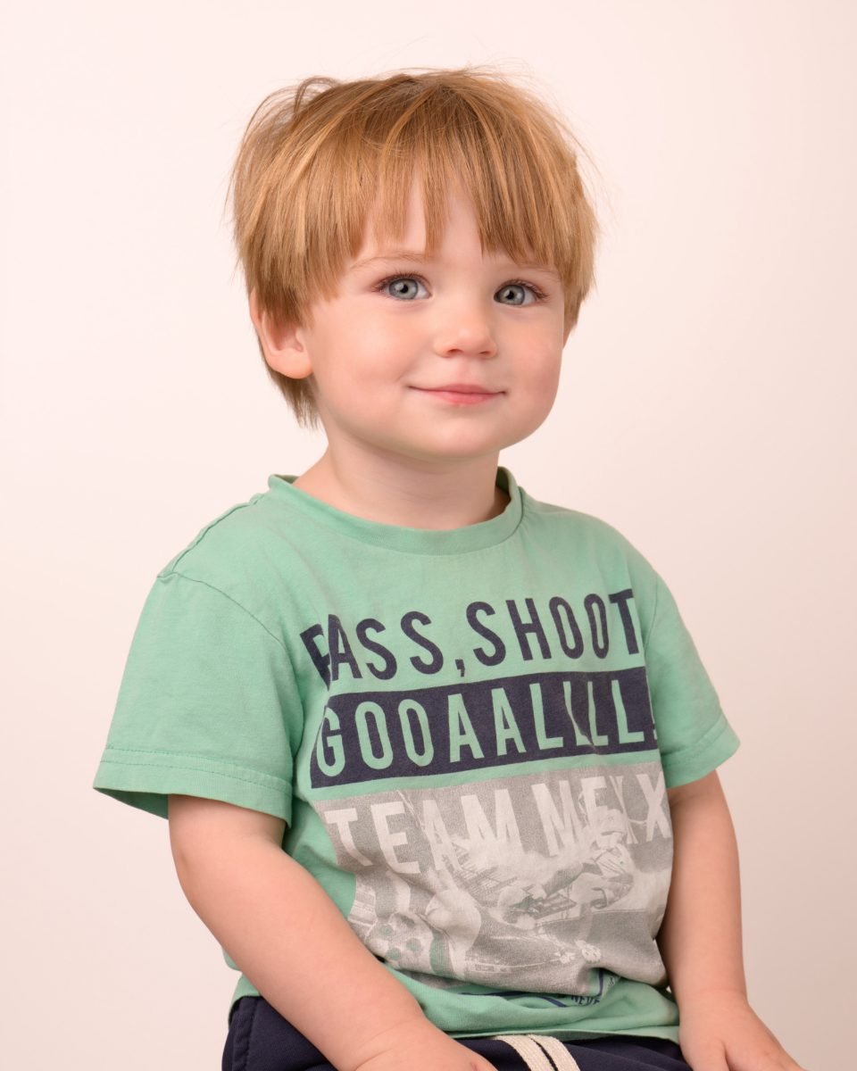 A red-haired boy in a green soccer tee smiling at the camera