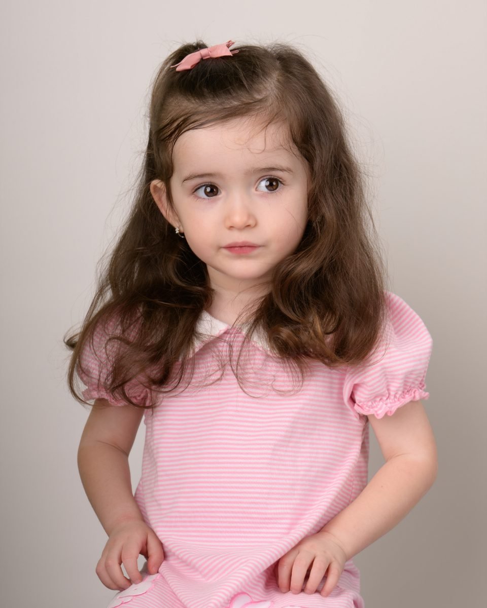 A girl in a pink striped top on a soft grey backdrop