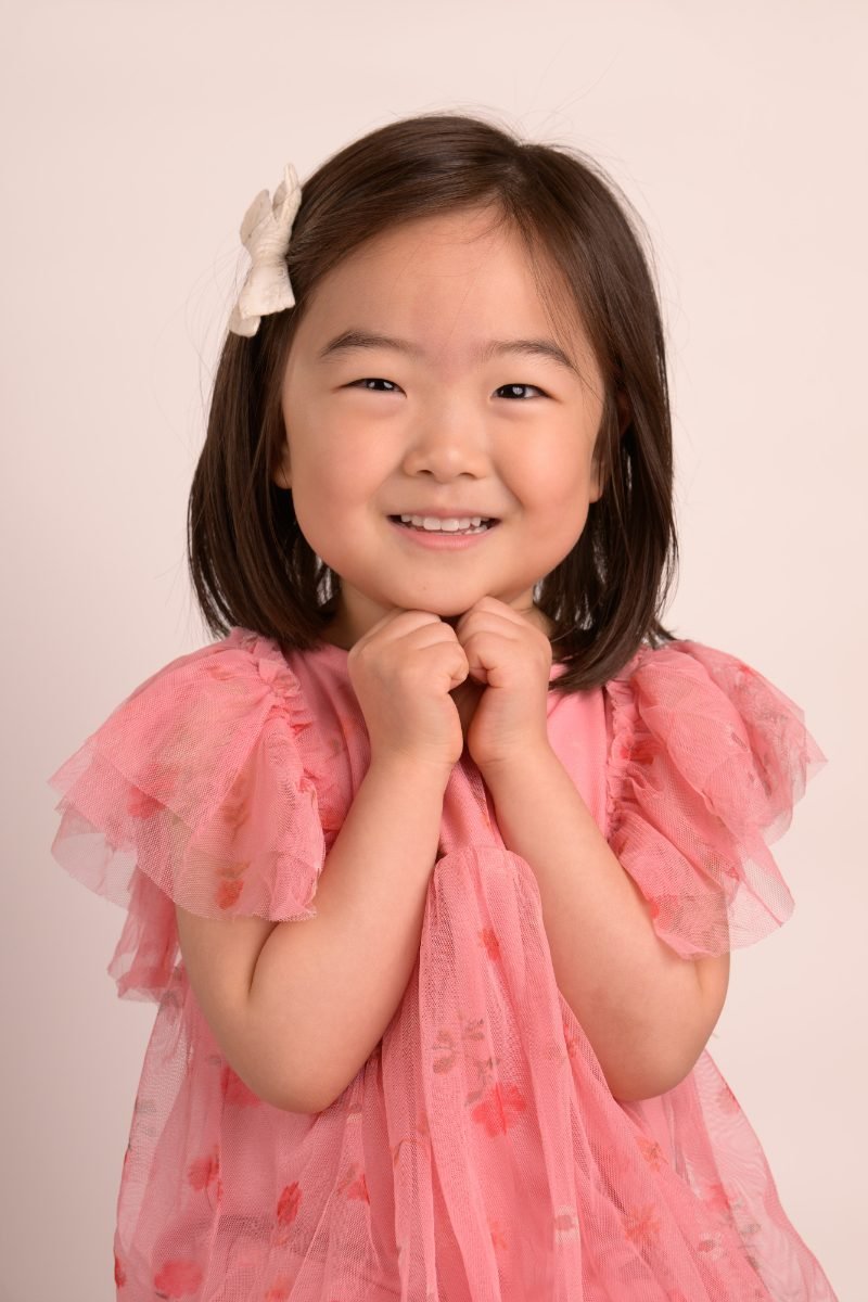 A girl in a pink ruffled top on a warm blush backdrop