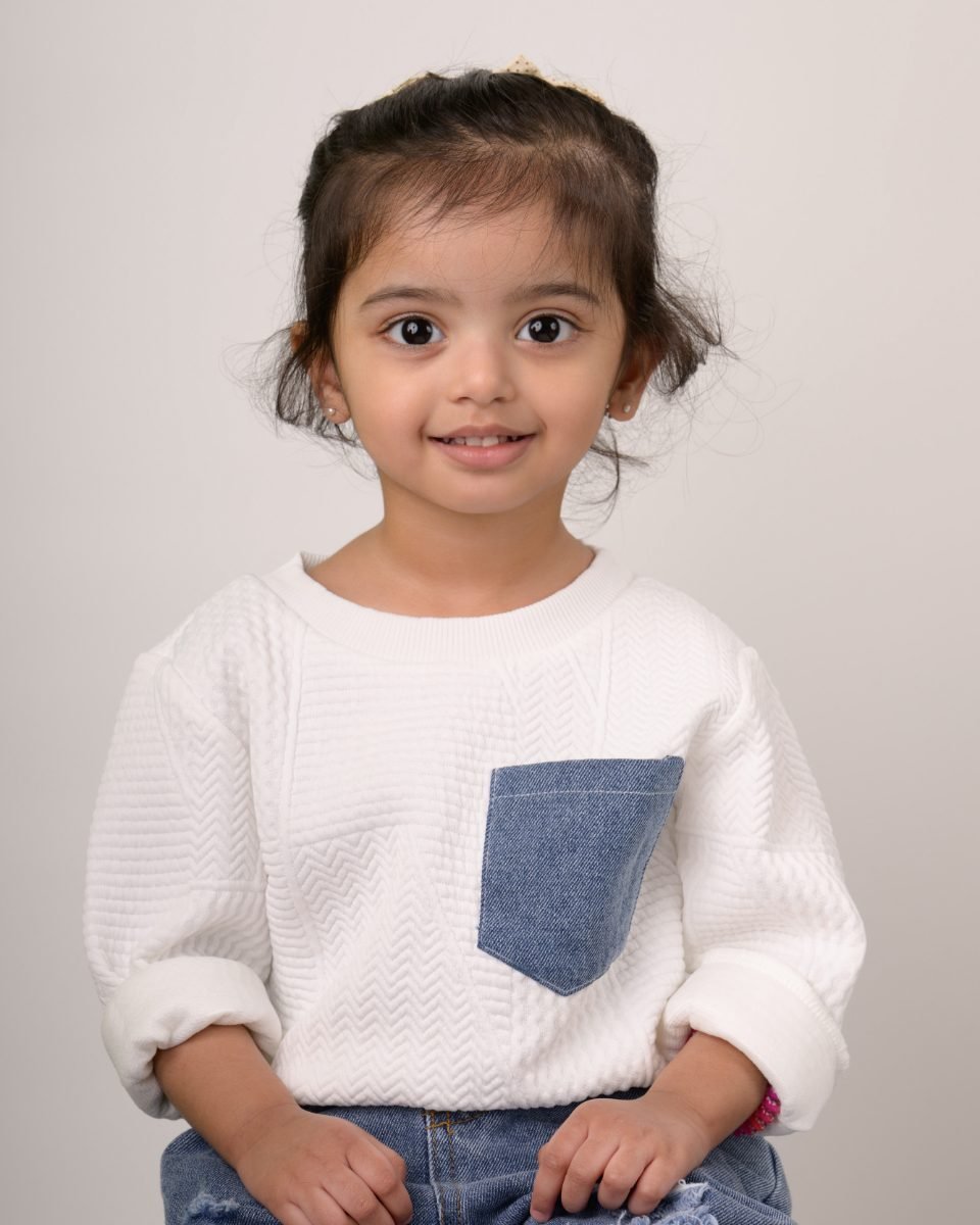 A girl in a white sweater with a denim pocket detail