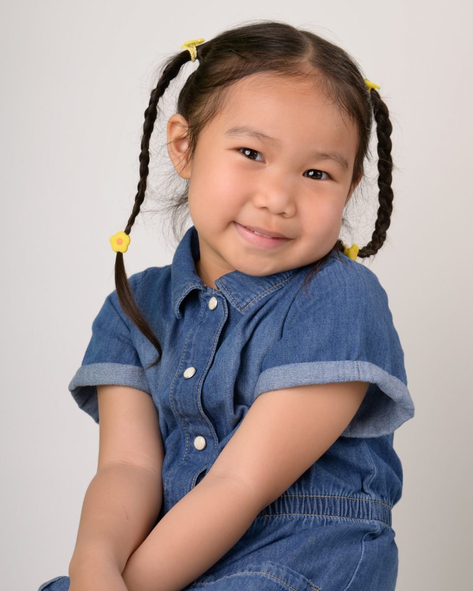 A girl with braids in a denim dress resting her hands at her chin