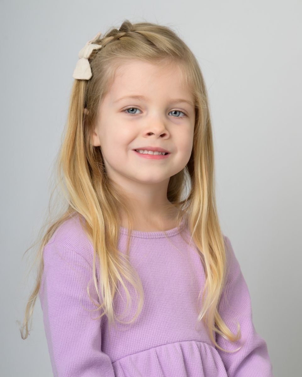 A girl in a lilac knit top on a soft grey backdrop