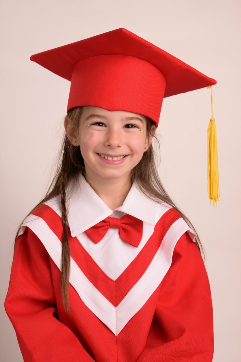 A preschool graduate in a red cap and gown with a white stole