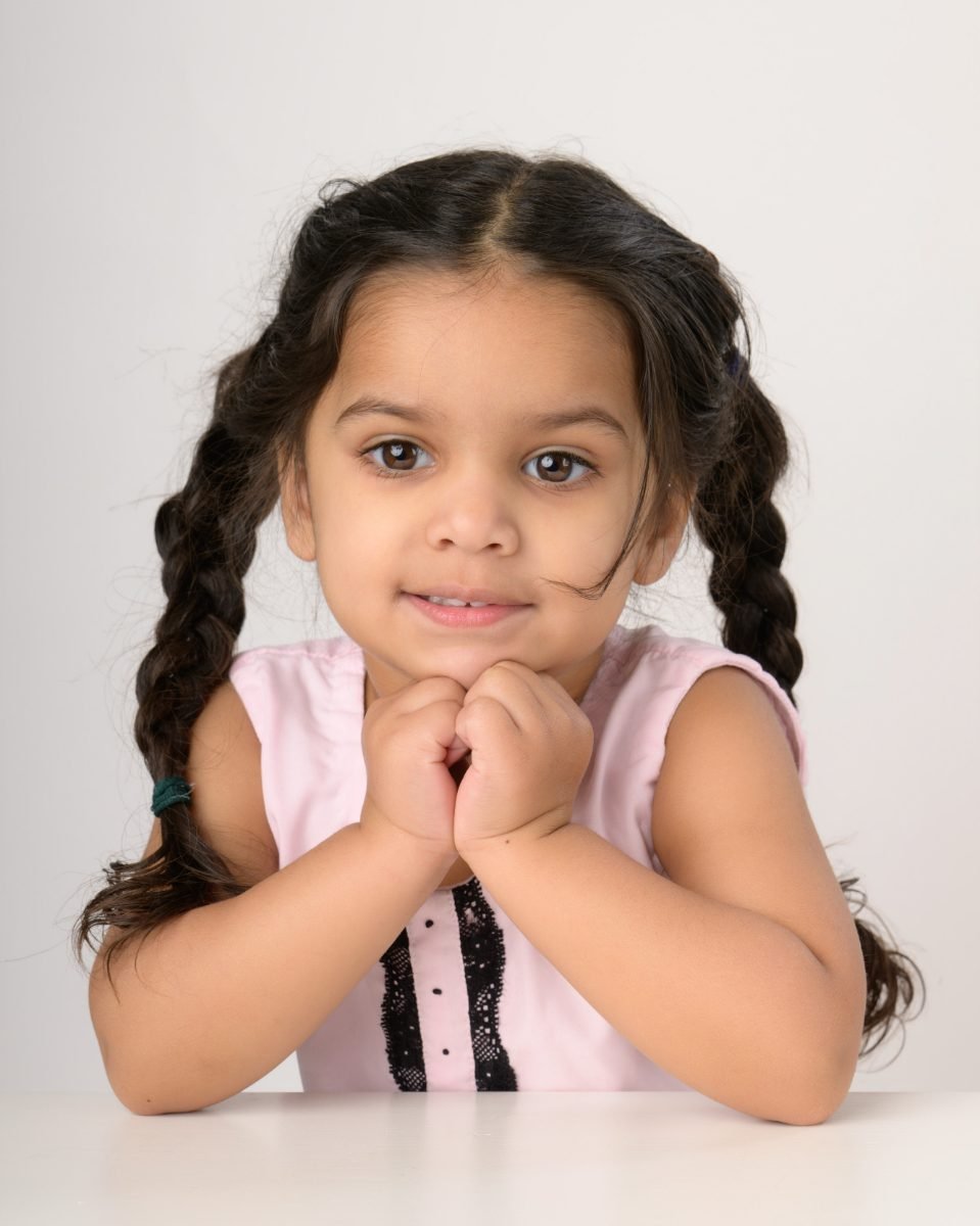 A girl with dark braids resting her chin on her clasped hands