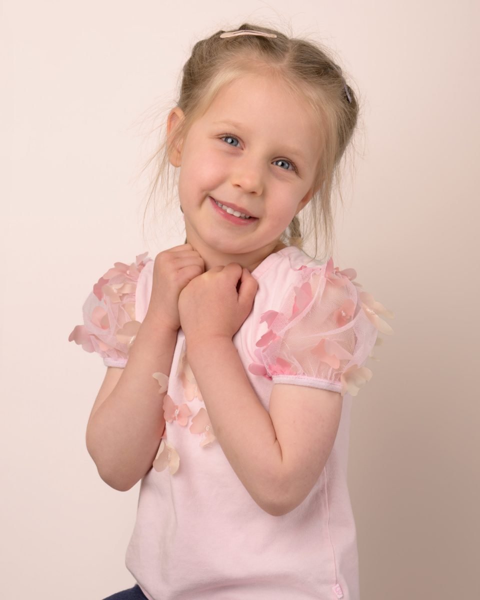 A girl in a pale pink puff-sleeve top with her hands clasped