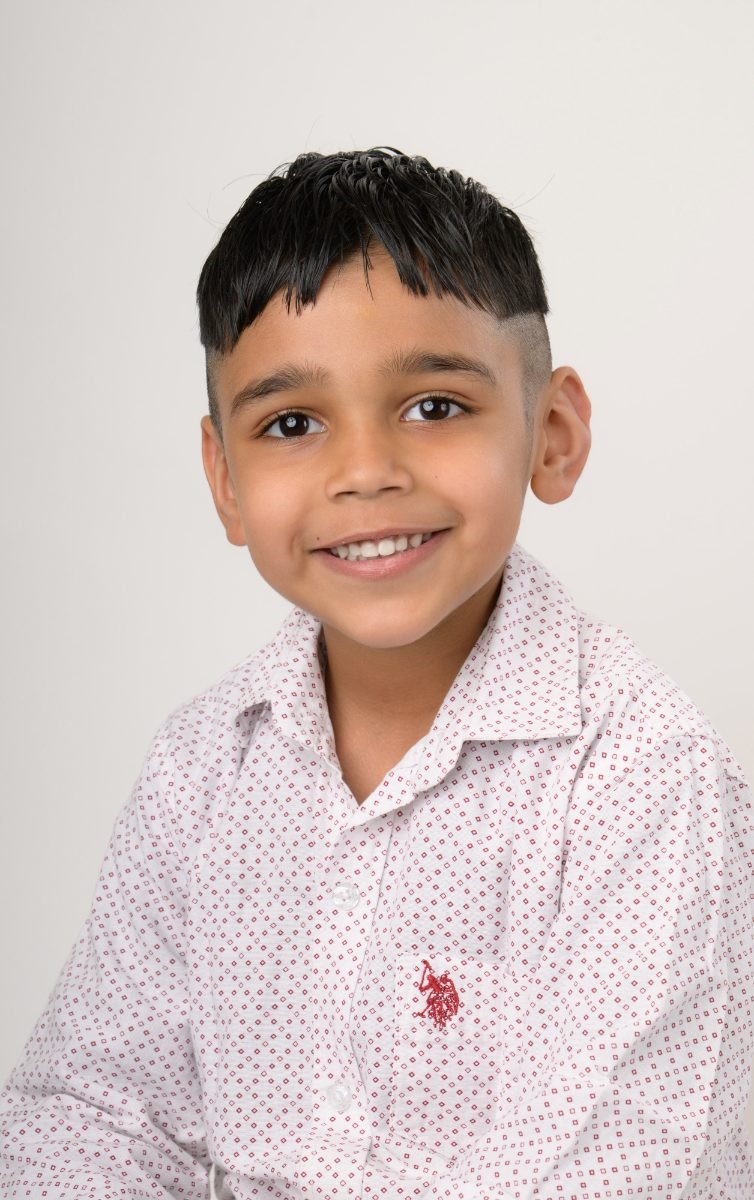 A boy in a white dotted shirt smiling at the camera
