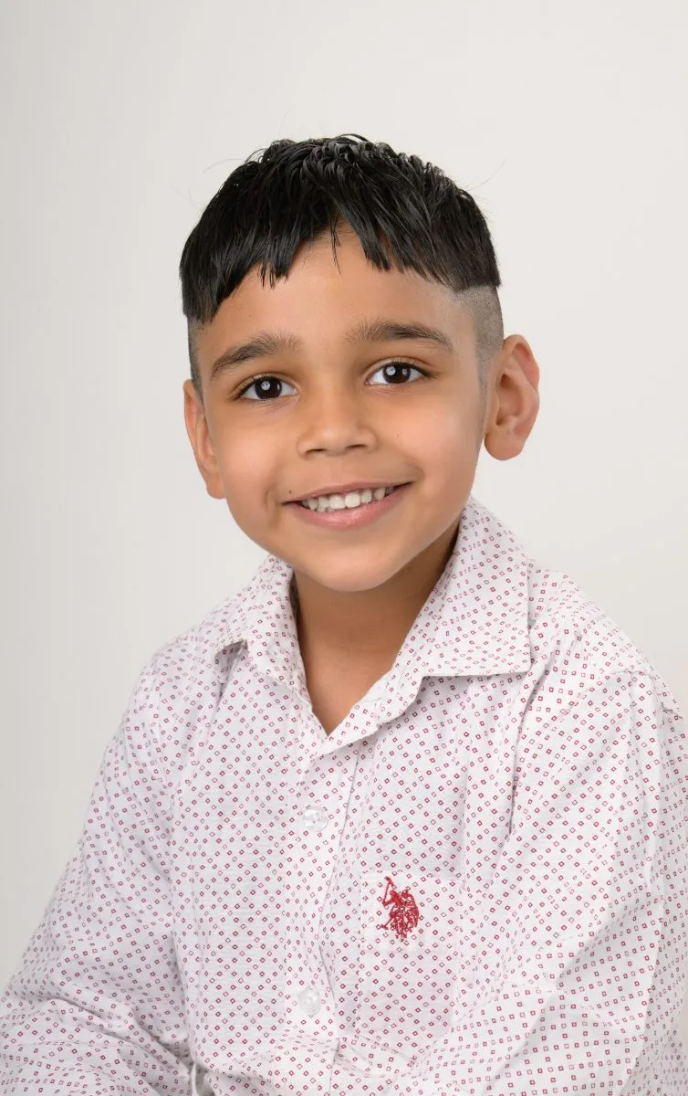 A boy in a white dotted shirt smiling at the camera