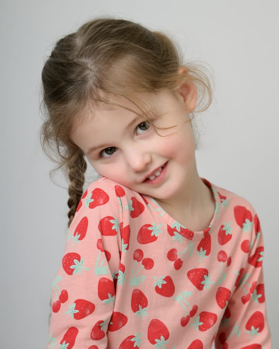 A girl in a strawberry-print top with her head tilted