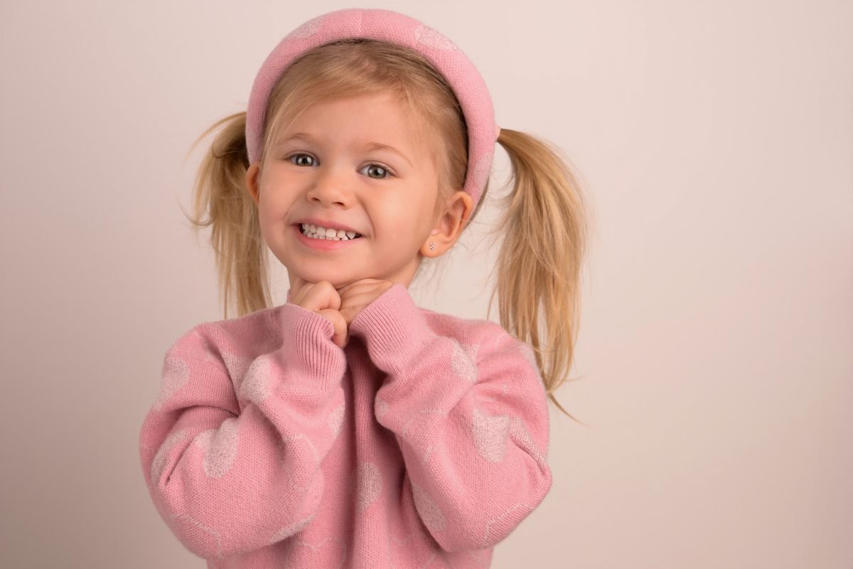 A girl with pigtails and a pink headband on a warm blush backdrop