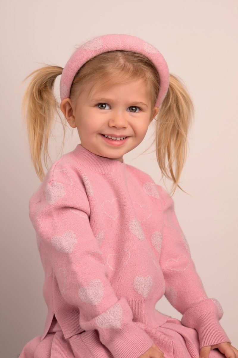 A girl with pigtails and a pink headband in a soft pink sweater