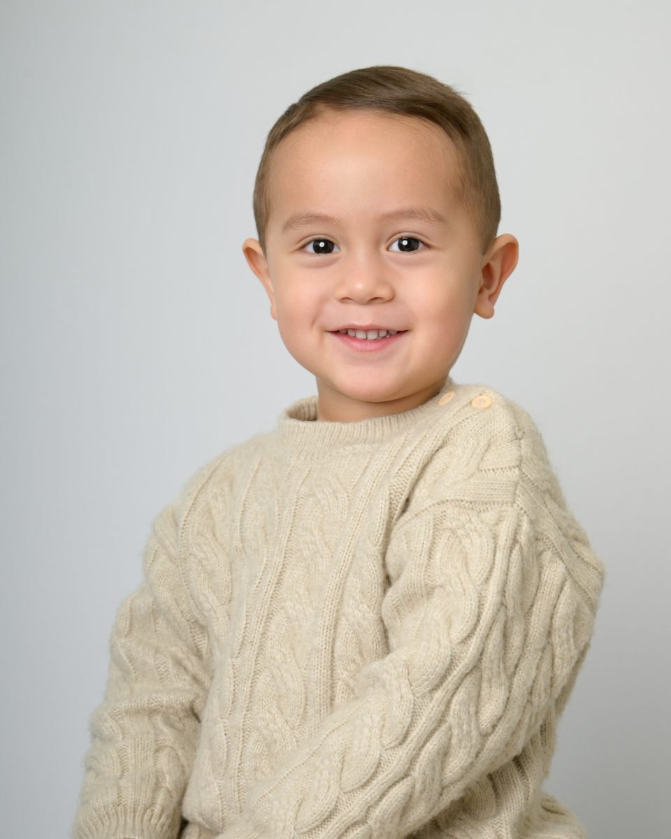 A boy in a cream cable-knit sweater smiling