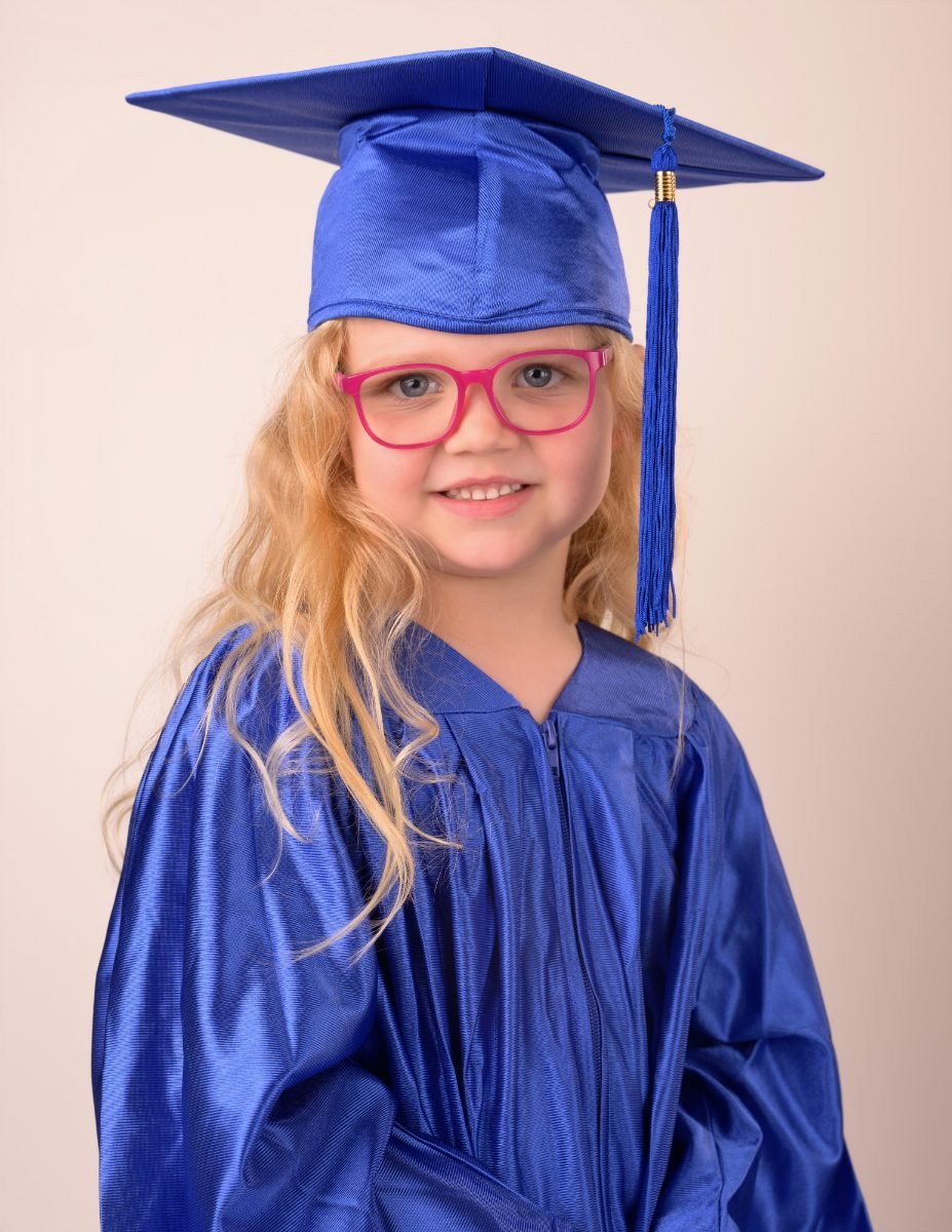 A preschool graduate in pink glasses and a royal blue cap and gown