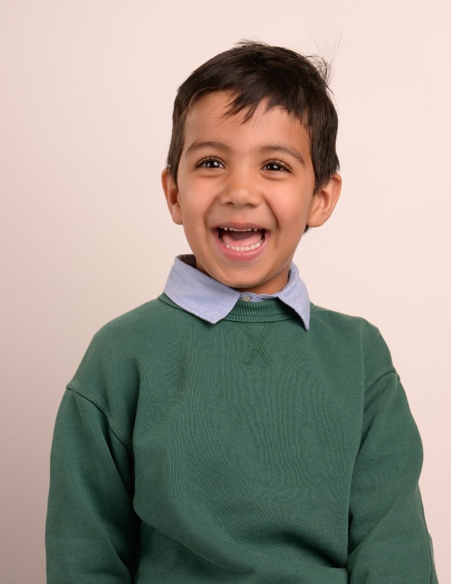A boy in a green sweater sticking his tongue out playfully