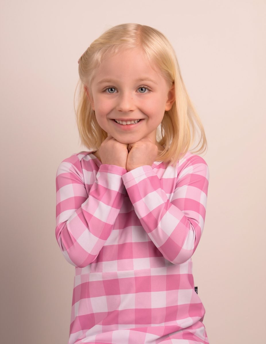 A girl in a pink gingham top with her hands clasped