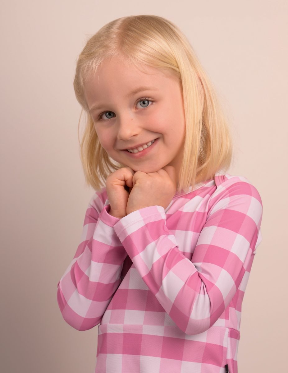 A girl in a pink gingham top on a soft grey backdrop