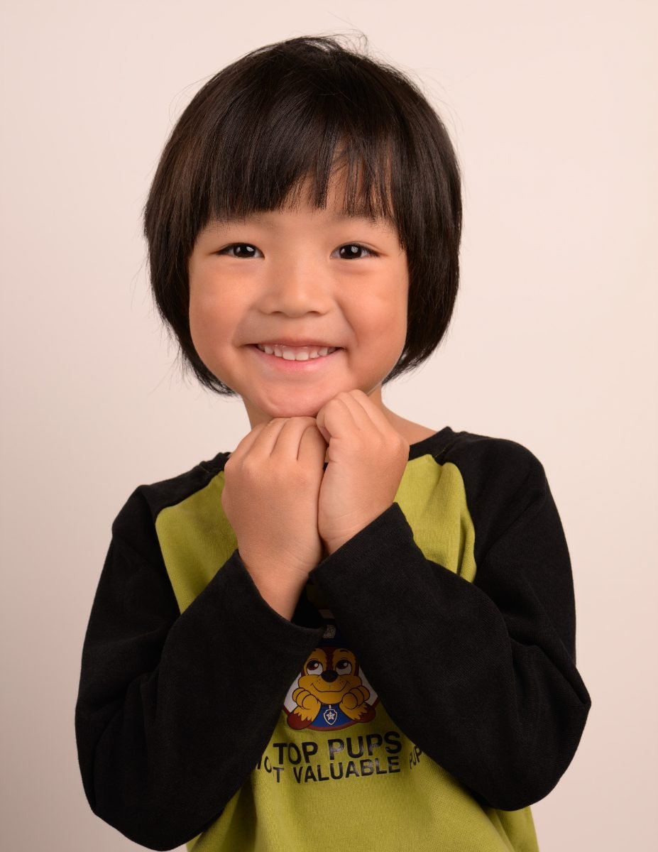 A preschool boy with a bob haircut, hands clasped under his chin