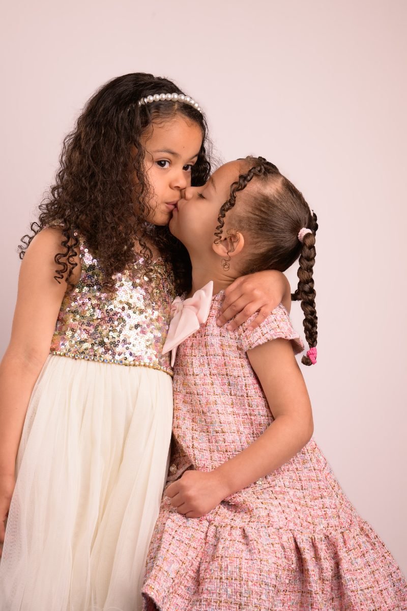 Two sisters in sequin dresses, one kissing the other on the cheek
