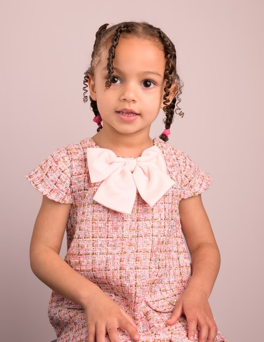 A preschool girl in a pink floral dress with a bow, hands together