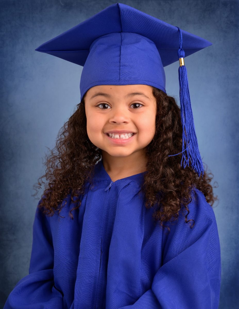 A preschool graduate with curly hair in a royal blue cap and gown