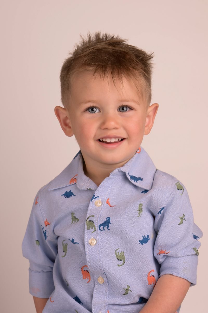 A boy in a dinosaur-print shirt with spiked hair, grinning