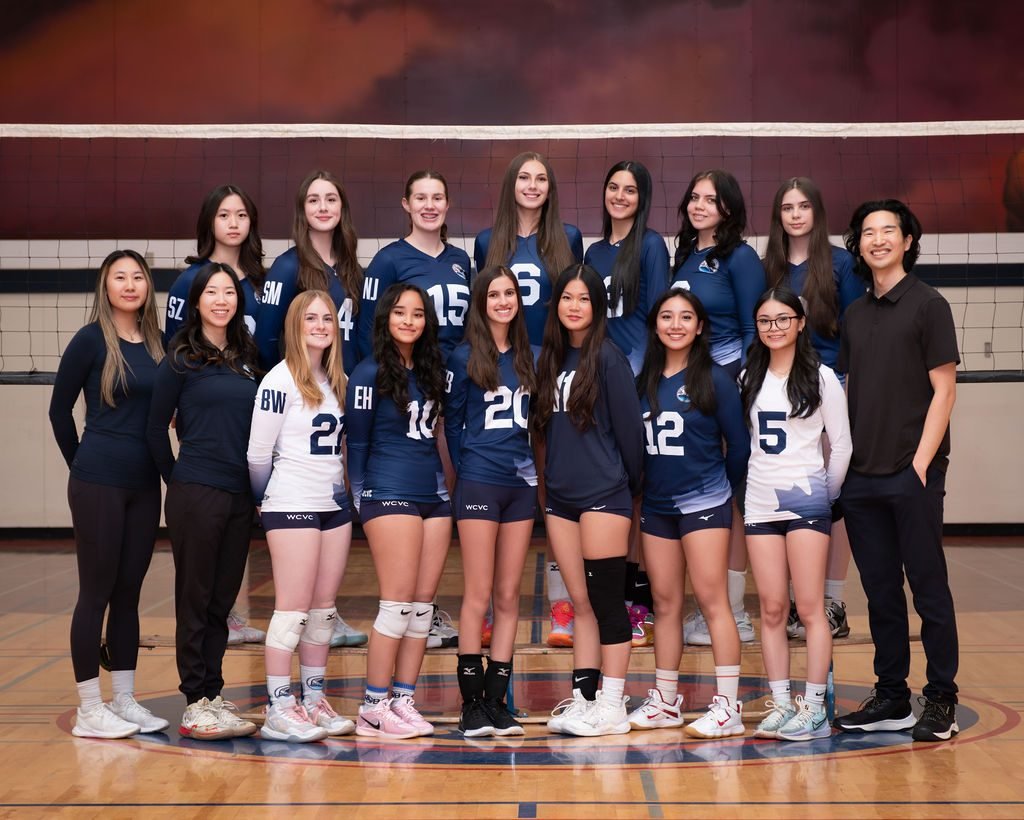 Volleyball team photo with athletes holding a game ball on the court